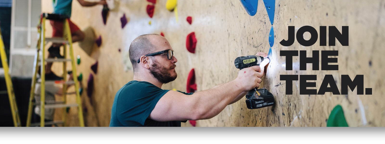Join the team. - Man drilling fixture into indoor rock climbing wall